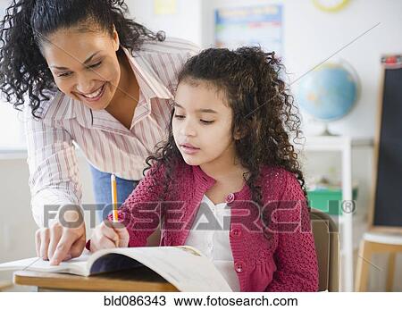 Stock Image - Teacher helping girl with school work in classroom. Fotosearch