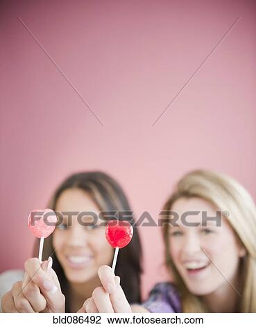Stock Image - Teenage girls holding heart-shape lollipops. Fotosearch