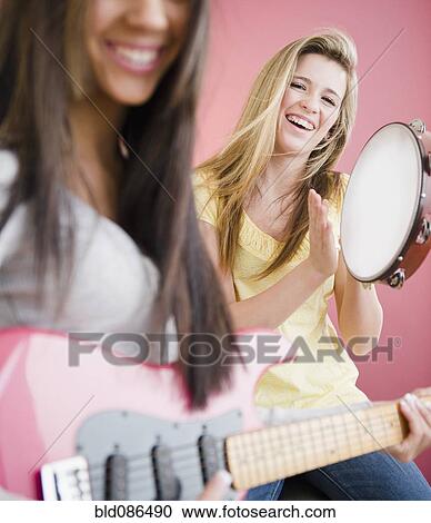 Stock Image - Teenage girls playing guitar and tambourine. Fotosearch