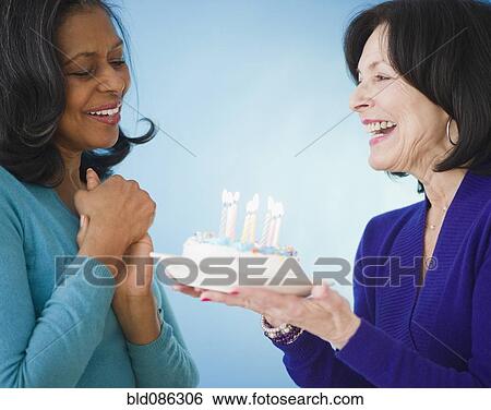 Stock Photograph - Woman surprising friend with birthday cake. Fotosearch