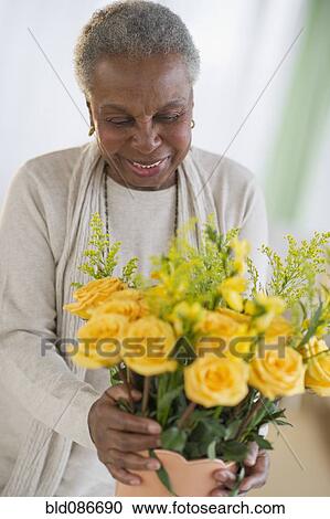 Stock Image - Black woman arranging roses in vase. Fotosearch