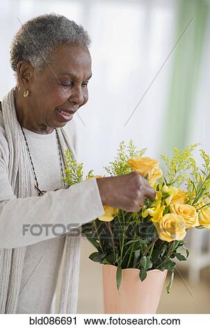 Stock Image - Black woman arranging roses in vase. Fotosearch