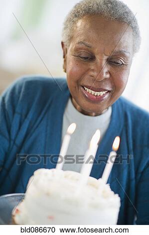 Stock Image - Black woman looking at birthday cake. Fotosearch