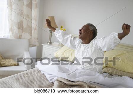 Stock Image - Black woman waking up in bed. Fotosearch