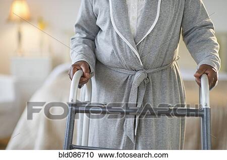 Stock Image - Black woman walking with walker in bedroom. Fotosearch