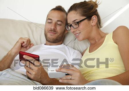 Stock Photo - Caucasian couple laying in bed with cell phones. Fotosearch