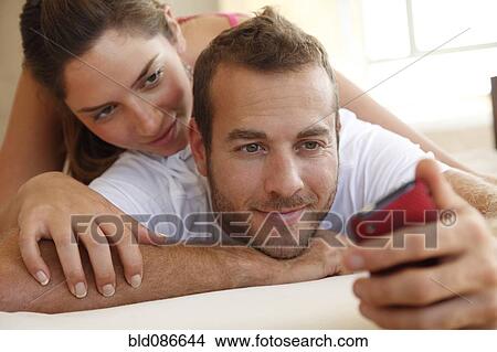 Picture - Caucasian woman watching husband using cell phone. Fotosearch