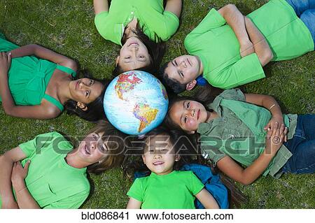 Stock Image - Children laying in grass around globe. Fotosearch