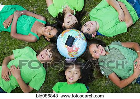 Stock Image - Children laying in grass around globe with solar panel. Fotosearch
