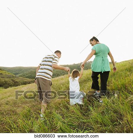 Stock Image - Family holding hands and walking up field. Fotosearch