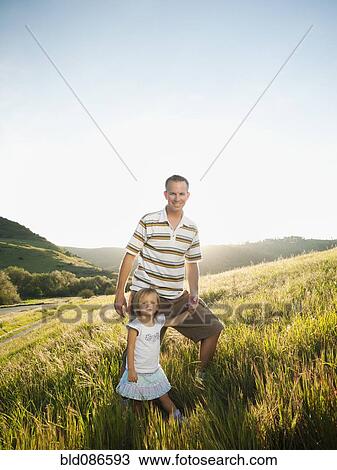 Stock Image - Father and daughter standing together in field. Fotosearch