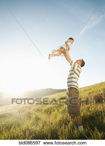 Stock Photo - Father standing in field lifting daughter. Fotosearch