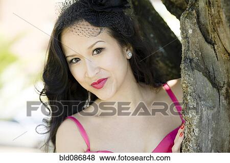 Stock Photo - Glamorous Asian woman standing near tree. Fotosearch