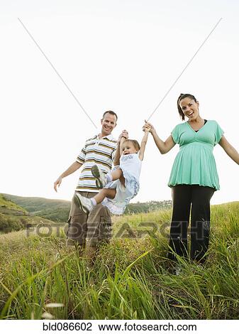 Stock Image - Happy parents swinging daughter in field. Fotosearch