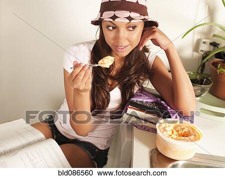 Stock Image - Hispanic woman eating ice cream and studying. Fotosearch