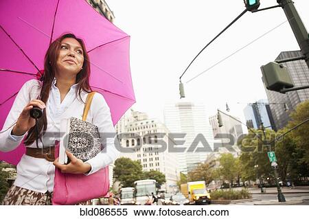 Stock Photography - Hispanic woman walking in city with umbrella. Fotosearch