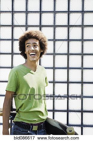 Stock Photo - Laughing mixed race teenager carrying skateboard. Fotosearch