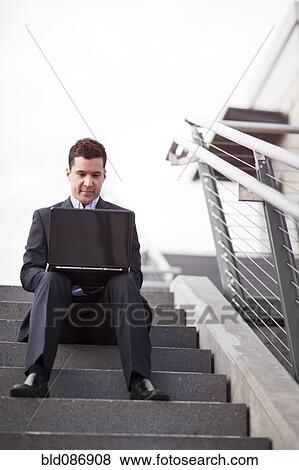 Stock Photo - Mixed race businessman sitting on steps using laptop. Fotosearch