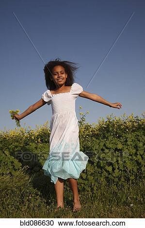 Stock Image - Mixed race girl holding flowers in field. Fotosearch