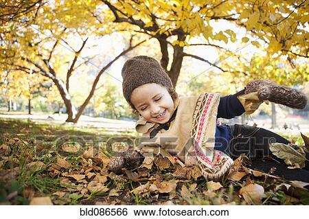 Stock Photograph - Mixed race girl laying in autumn leaves. Fotosearch