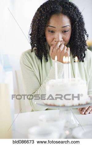 Stock Image - Mixed race woman looking at birthday cake. Fotosearch