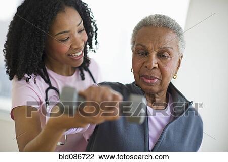 Stock Image - Nurse helping woman exercise with dumbbell. Fotosearch