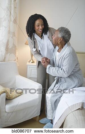 Stock Photo - Nurse helping woman get out of bed. Fotosearch
