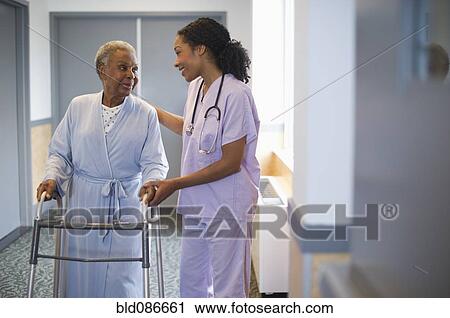 Nurse helping woman use walker in hospital hallway View Large Photo Image Stock Image - Nurse helping woman use walker in hospital hallway. Fotosearch