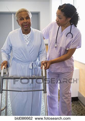Stock Image - Nurse helping woman use walker in hospital hallway. Fotosearch