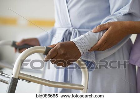 Stock Photography - Nurse helping woman use walker in hospital hallway. Fotosearch