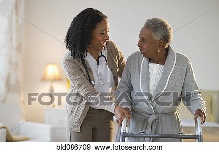 Stock Photo - Nurse helping woman walk with walker. Fotosearch