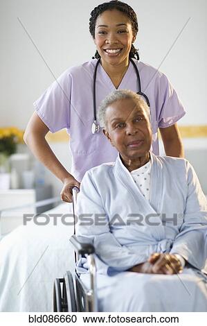 Stock Image - Nurse pushing woman sitting in wheelchair in hospital. Fotosearch