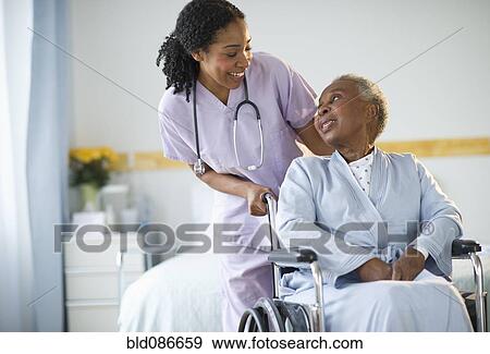 Stock Photo - Nurse pushing woman sitting in wheelchair in hospital. Fotosearch