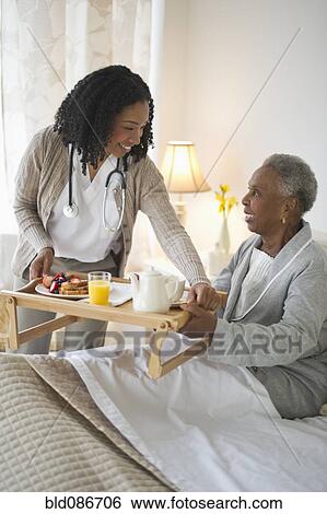 Stock Photograph - Nurse serving woman breakfast in bed. Fotosearch