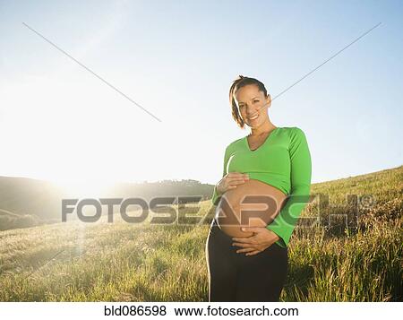 Stock Photo - Pregnant Hispanic woman caressing stomach in field. Fotosearch