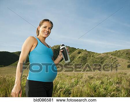 Stock Image - Pregnant Hispanic woman drinking water in remote area. Fotosearch