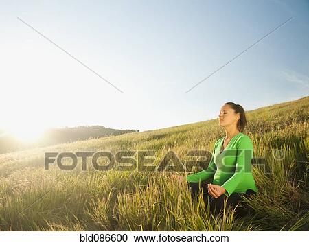 Stock Image - Pregnant Hispanic woman practicing yoga in field. Fotosearch