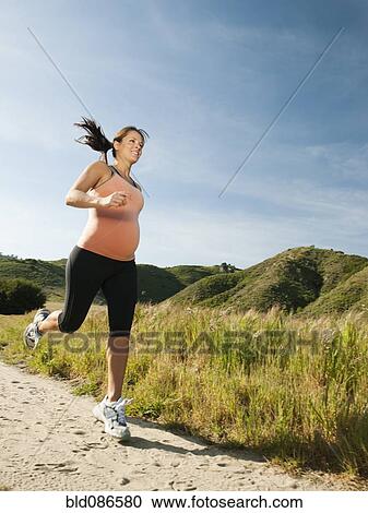 Stock Image - Pregnant Hispanic woman running in remote area. Fotosearch