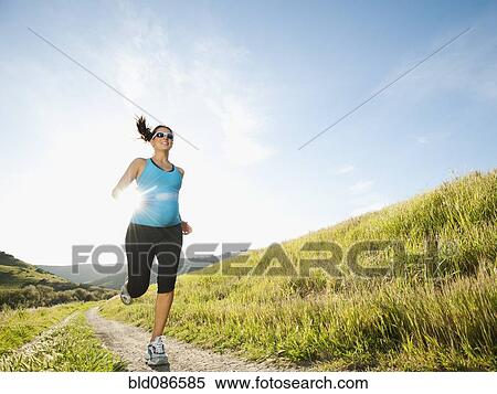 Stock Photography - Pregnant Hispanic woman running in remote area. Fotosearch