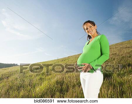 Stock Image - Pregnant Hispanic woman standing in field. Fotosearch