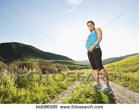 Stock Photo - Pregnant Hispanic woman standing in remote area. Fotosearch
