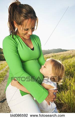 Stock Image - Pregnant mother hugging daughter outdoors. Fotosearch