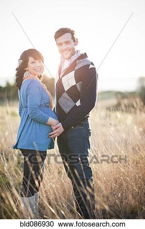 Stock Image - Pregnant woman holding husband's hands in field. Fotosearch