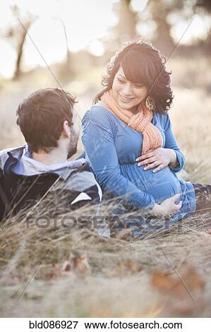 Stock Photo - Pregnant woman sitting in field with husband. Fotosearch
