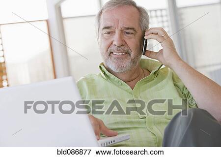 Stock Photo - Senior Chilean man using laptop and cell phone. Fotosearch