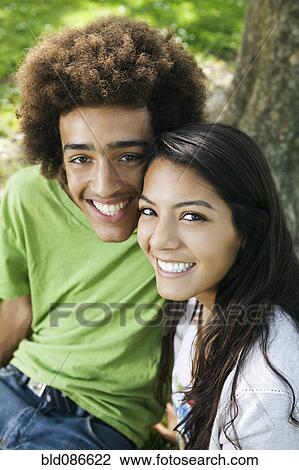 Stock Image - Smiling teenage couple sitting outdoors. Fotosearch