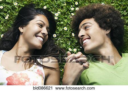 Stock Image - Teenage couple laying in grass holding hands. Fotosearch