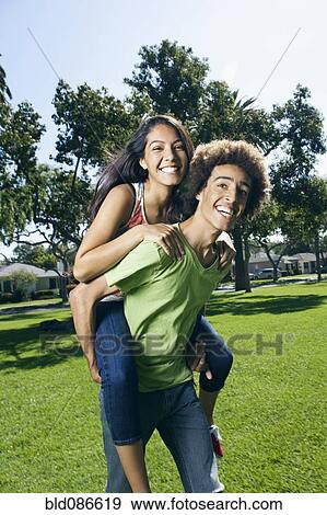 Stock Photo - Teenager carrying girlfriend on his back in park. Fotosearch