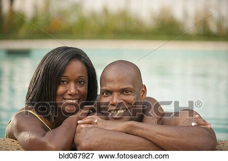 Stock Photo - African American couple leaning on edge of swimming pool. Fotosearch