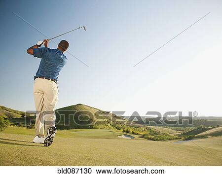 Stock Image - Black golfer swinging golf club. Fotosearch